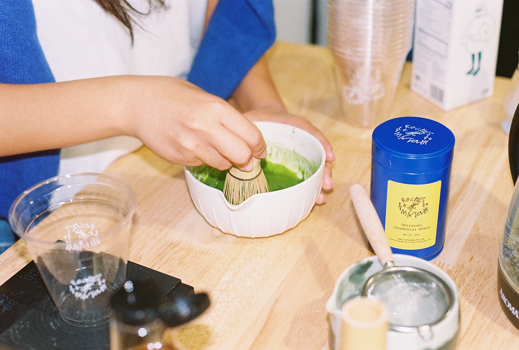 Film photo of matcha being whisked next to a rocky's matcha tin
